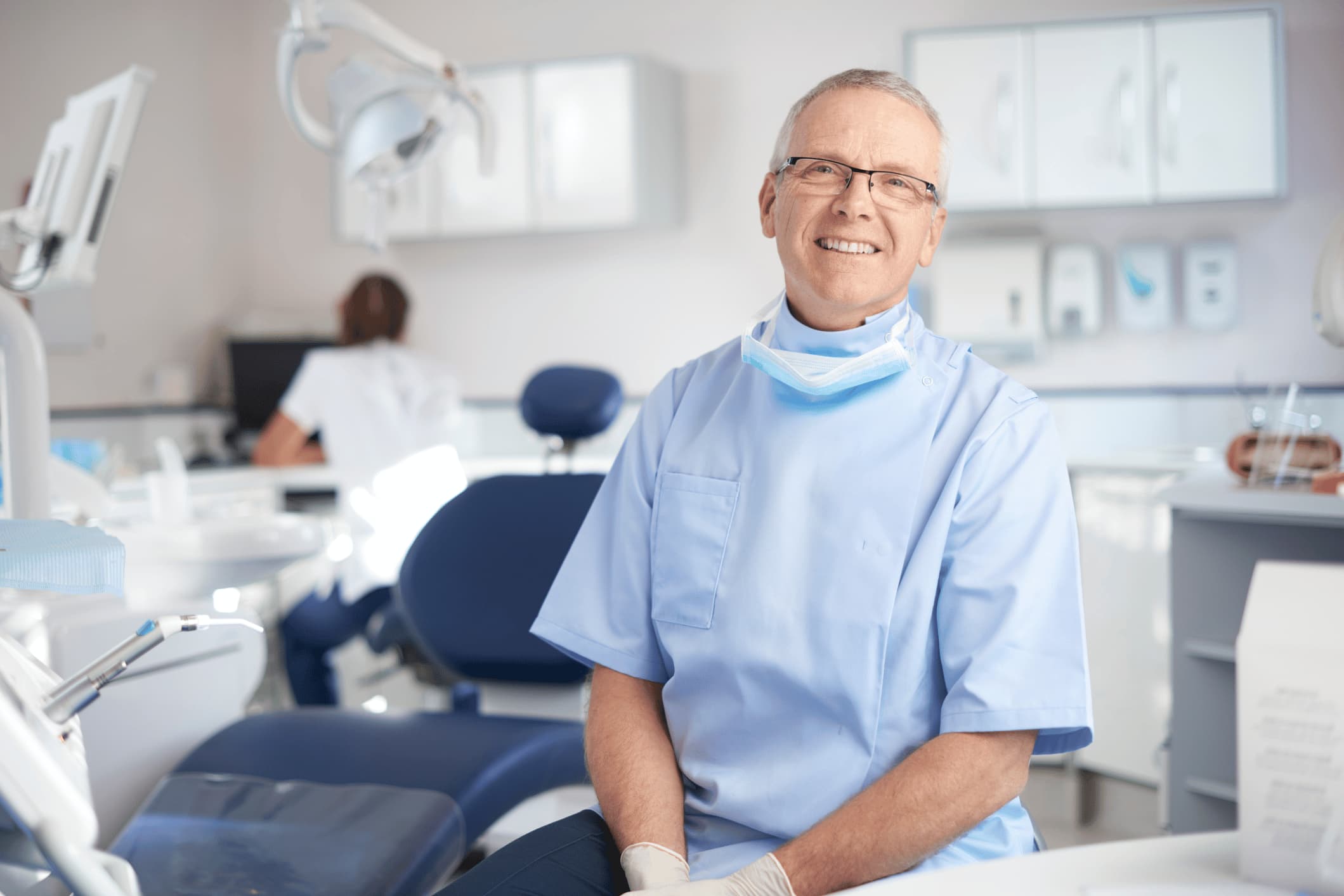 A male dentist sitting in his surgery smiling at the camera.