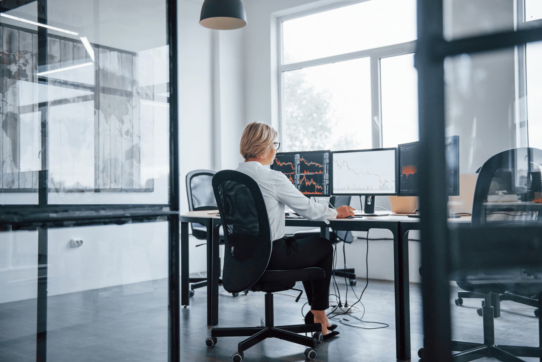 Female stockbroker working at a desk with three screens.