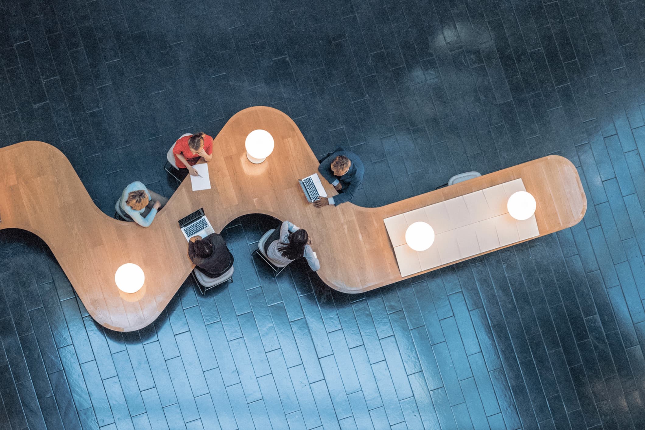 Top-down view of five people working at a curved desk.