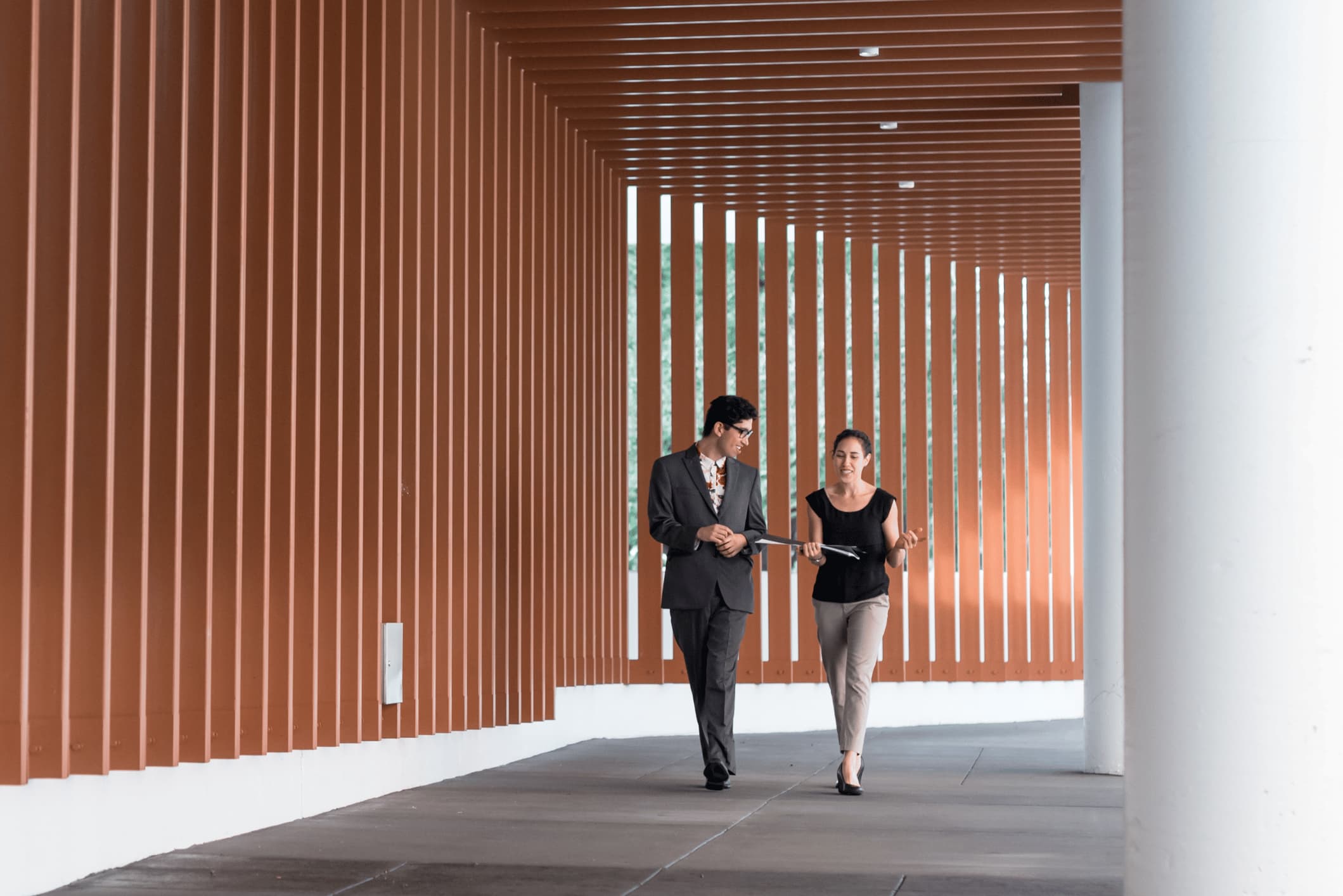 Two colleagues walking through an outdoor corridor while talking.
