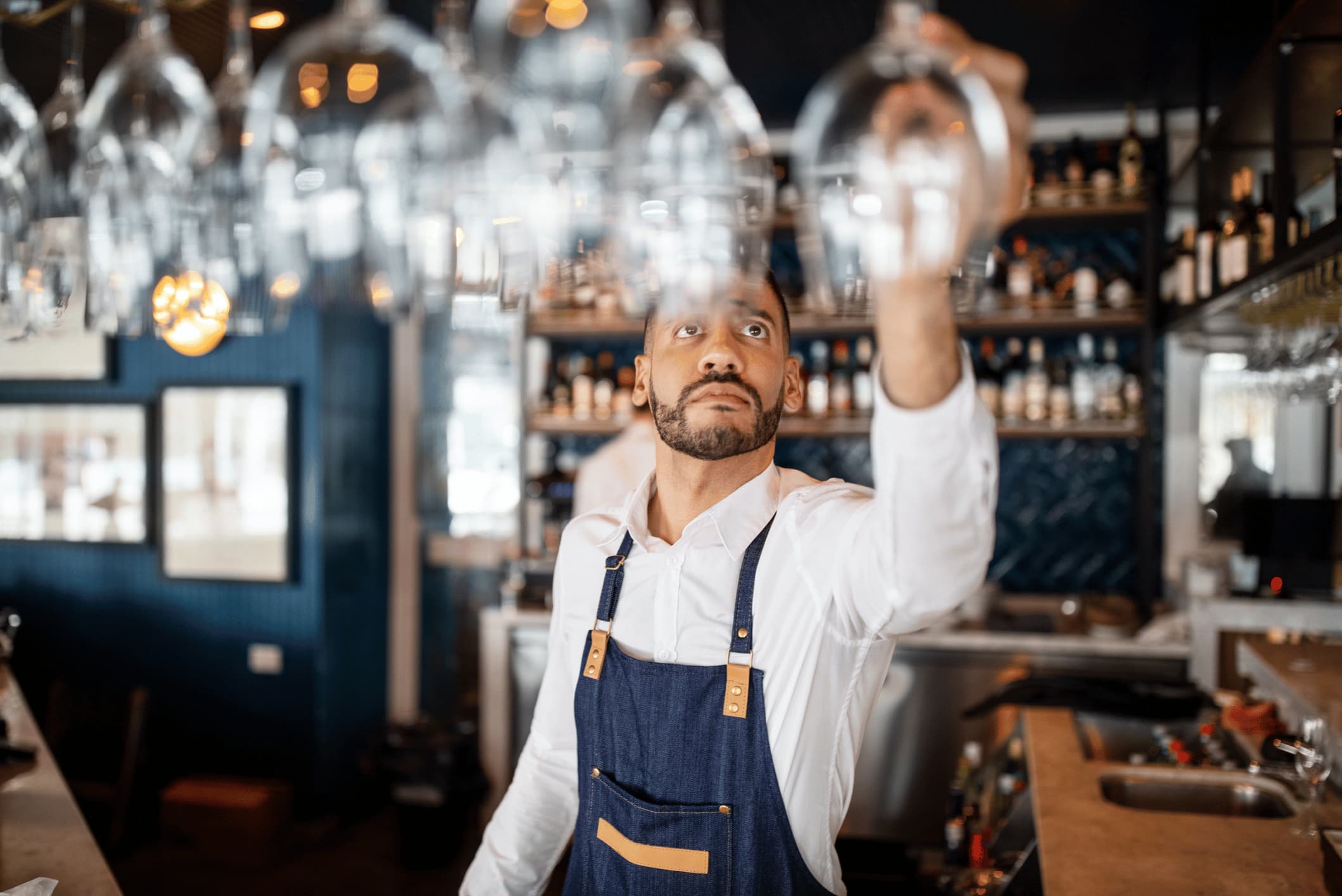 Bartender reaching for a wine glass hanging from a rack.