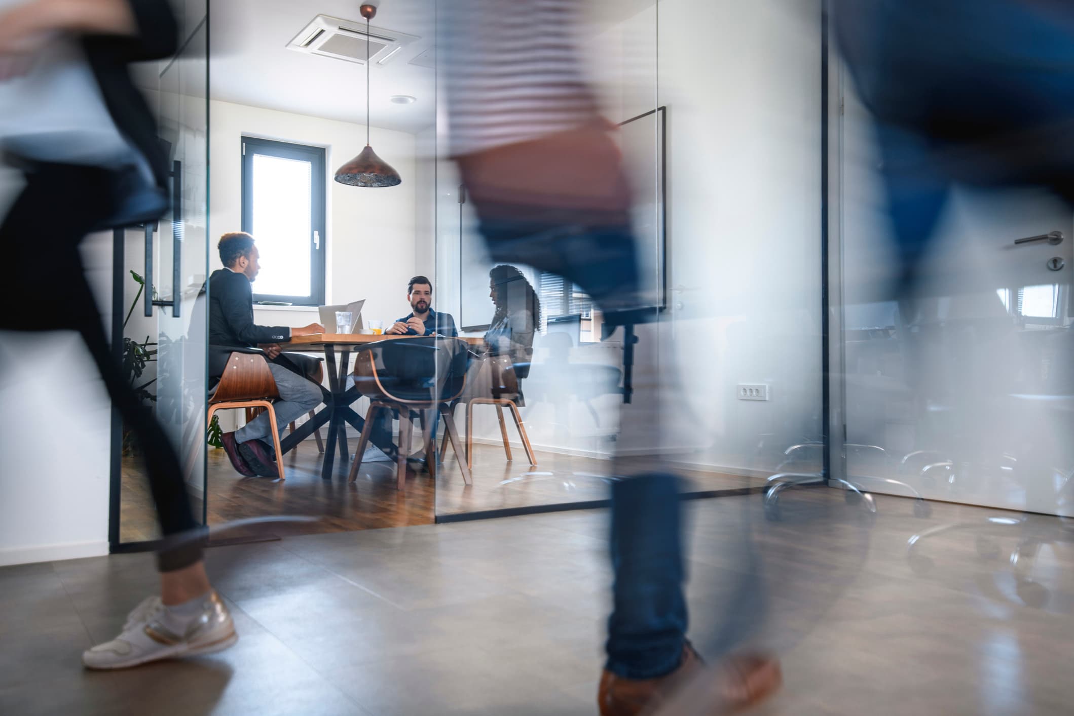 Blurred motion of office workers walking in front of a meeting room.