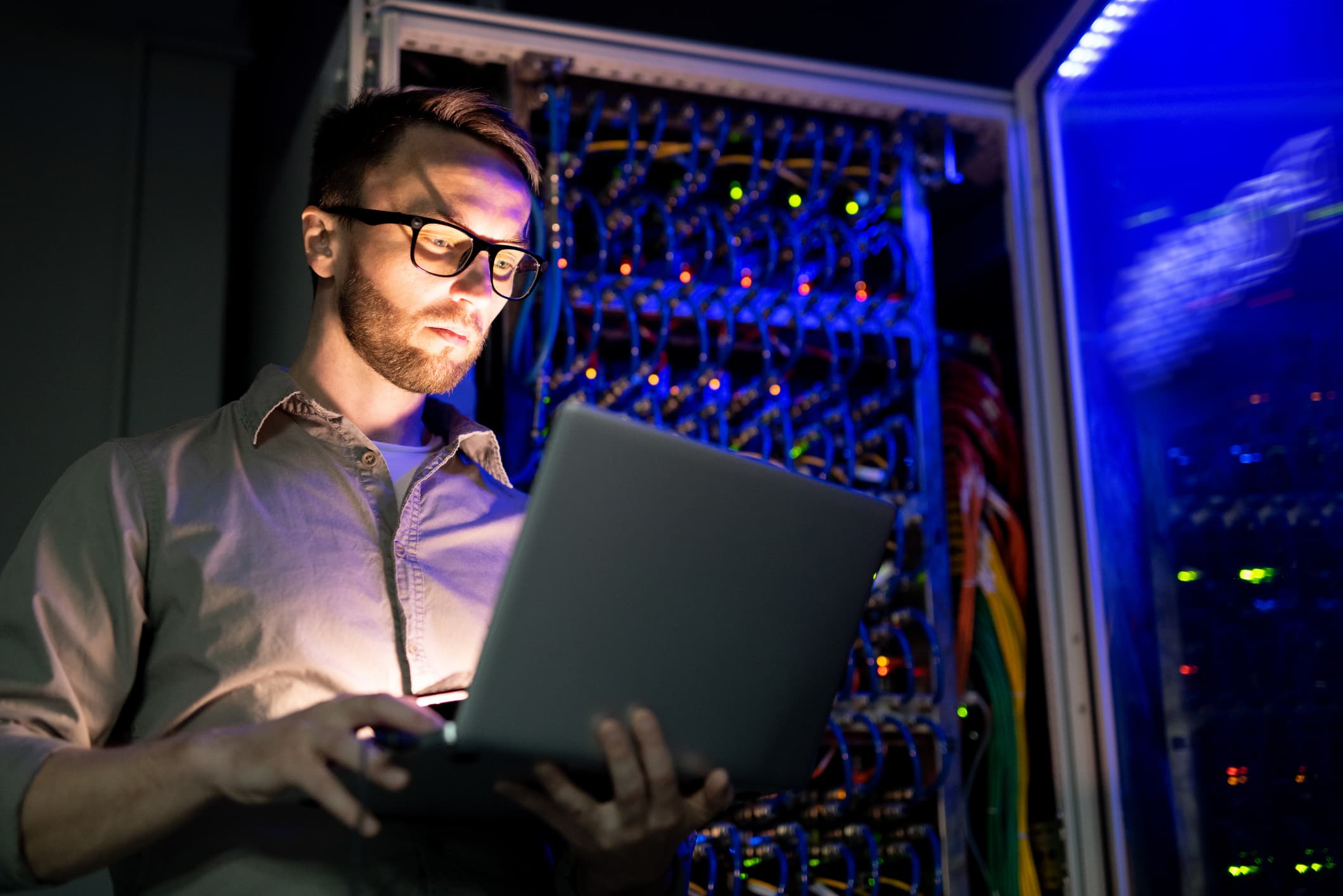Man looking at a laptop while in a server room.