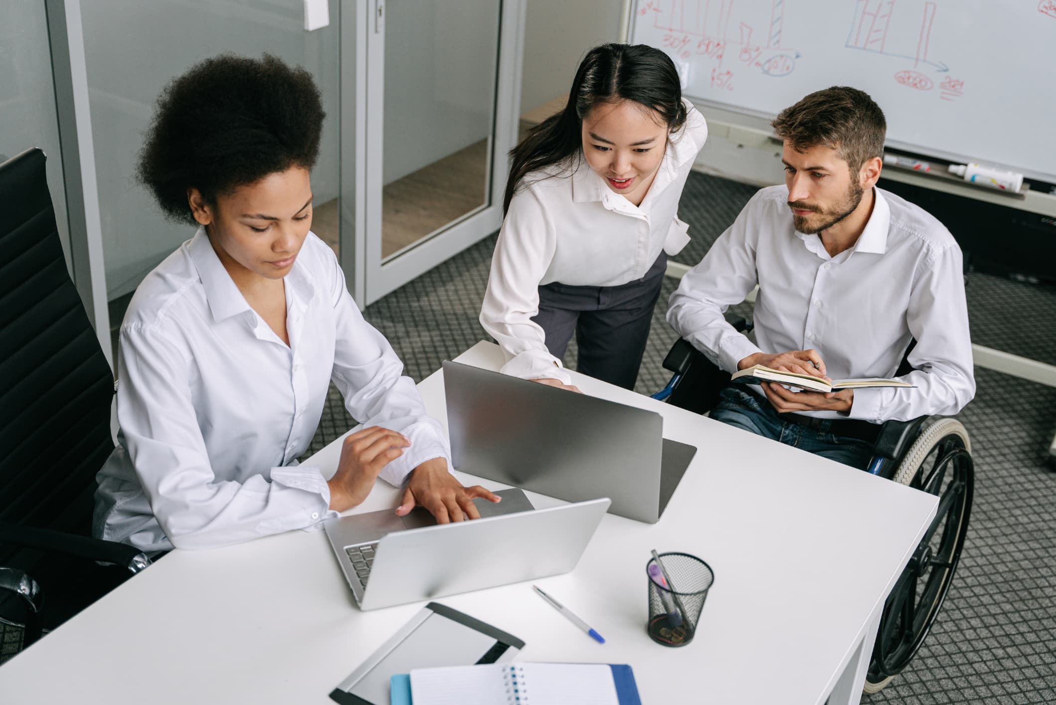 Three people sitting around a desk looking at two laptops.